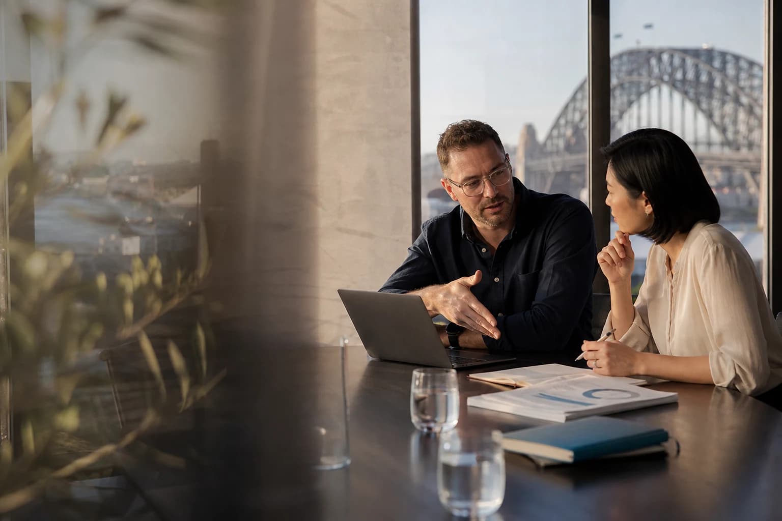 Two senior consultants in a Sydney boardroom reviewing an AI strategy with the harbour visible through the window