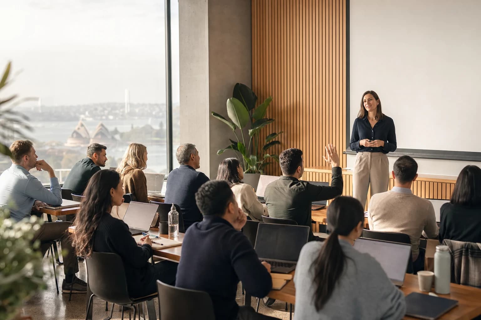 Enterprise AI training session in a contemporary Sydney corporate learning centre, instructor at the front, business professionals engaged at laptops